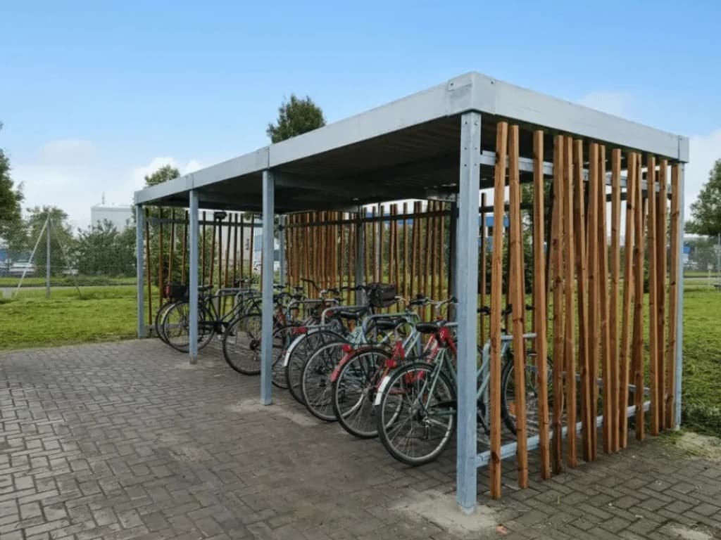 Abri vélo design en métal et bois avec plusieurs vélos stationnés sur un sol pavé, idéal pour les entreprises et collectivités, réalisé par Bycommute.