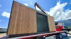Abri vélo ByCommute basé sur un container maritime en bois, en cours de transport sur une remorque de camion.