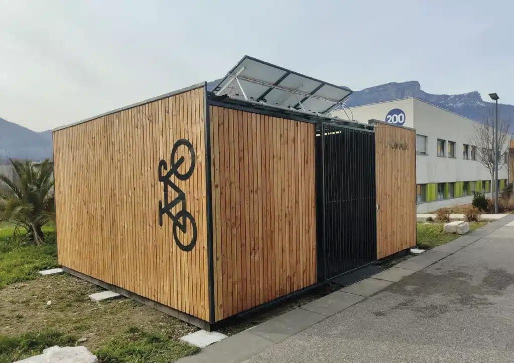 Consigne à vélos en bois fermée de ByCommute, équipée de panneaux solaires sur le toit, installée à l'extérieur. Cet abri vélo sécurisé et écologique offre une protection optimale pour les vélos tout en utilisant l'énergie solaire.