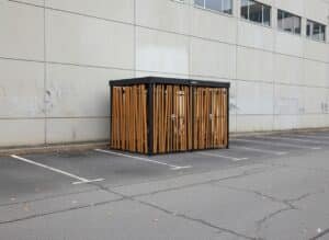 Abri vélo fermé design de la marque Bycommute, installé sur un parking d’entreprise, avec habillage en lames de bois verticales.