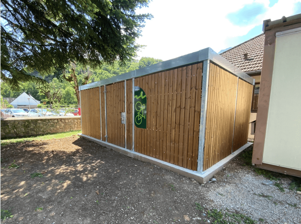 Abri vélo bois fermé avec structure métallique, installé dans un espace extérieur arboré, idéal pour le stationnement sécurisé de vélos.