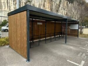 Abri vélo bois avec toiture équipée de panneaux solaires, installé sur un parking au pied d’une falaise, conçu par ByCommute pour une collectivité ou une entreprise