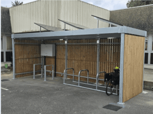 Abri vélo design en bois avec structure métallique galvanisée, équipé d'un rack à vélos, installé dans une cour d'entreprise, un vélo y est stationné.