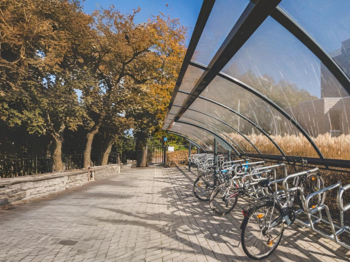 Abri vélo design en extérieur avec toiture courbe en polycarbonate et supports métalliques, installé dans un espace arboré.