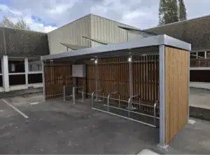 Abri vélo bois et métal avec arceaux de stationnement, installé sur un parking d'entreprise, solution design et sécurisée pour le stationnement vélo.