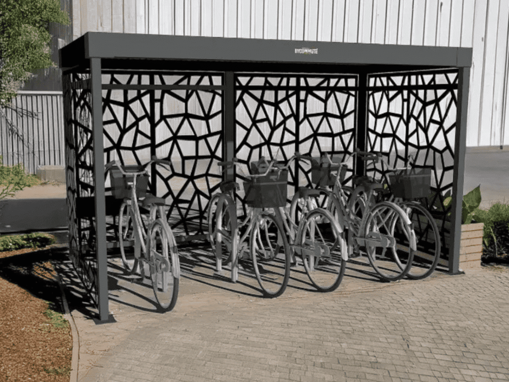 Bycommute design cykelskur i sort metal, installeret udenfor på en asfalteret overflade, med geometriske vægge og flere parkerede cykler.